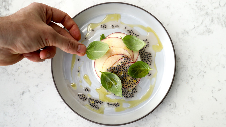 A chef garnishing a dish with basil