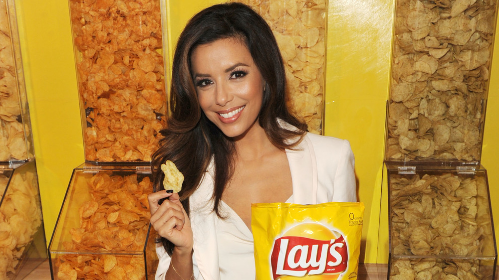 Eva Longoria in white jacket and shirt holding a potato chip and Lay's potato chip bag