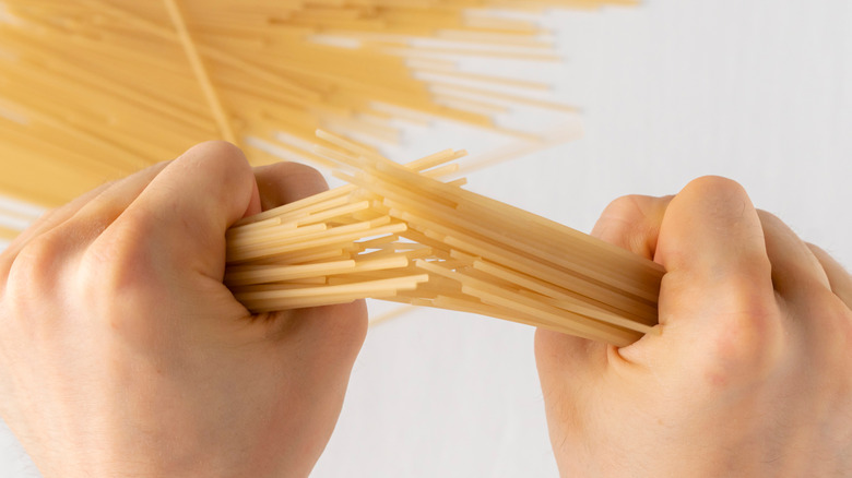 two hands breaking uncooked spaghetti