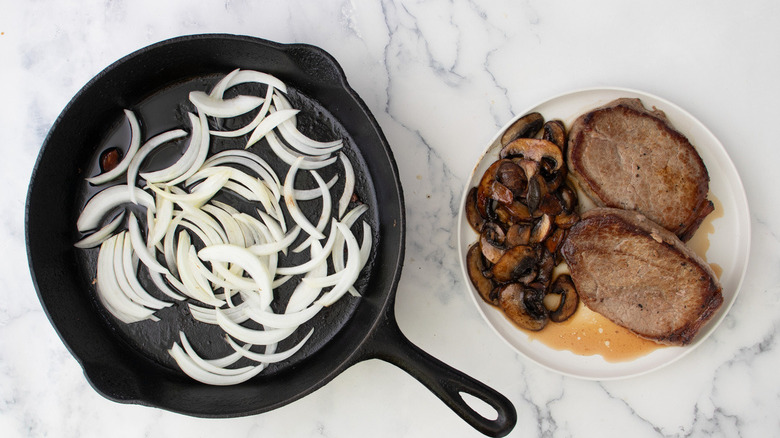 onions in skillet next to steaks