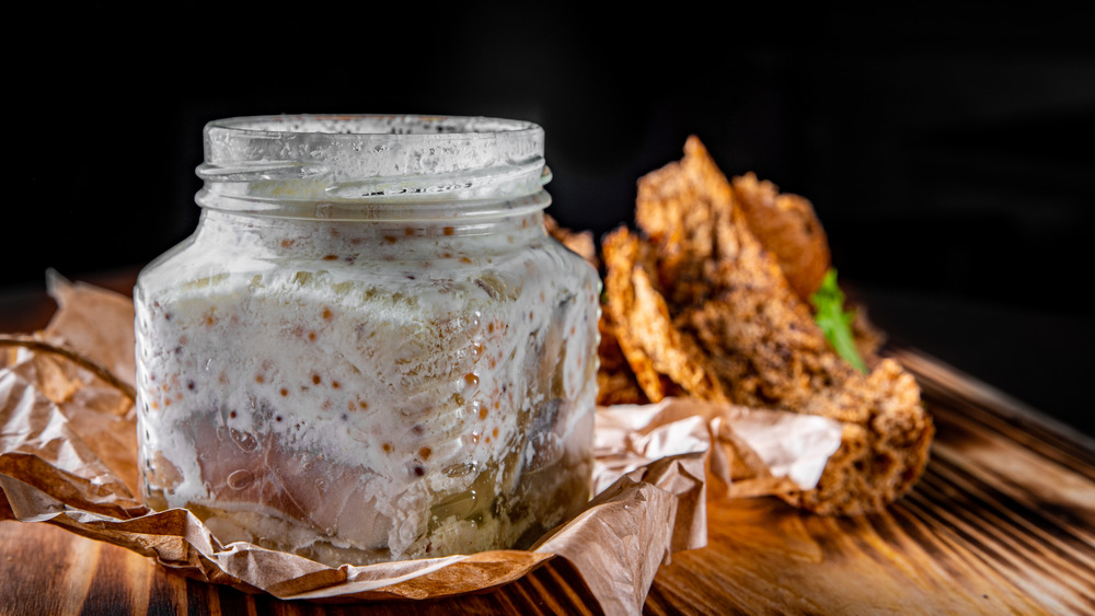 Cream and pickle herring in a jar on brown crumpled paper