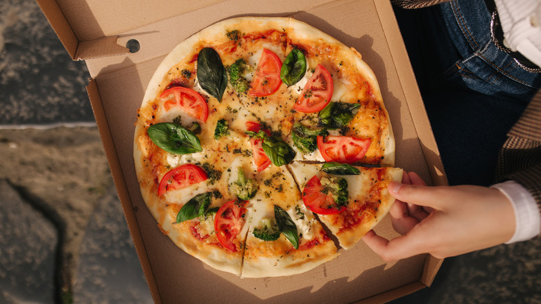 Hands holding a pizza box and reaching for a slice