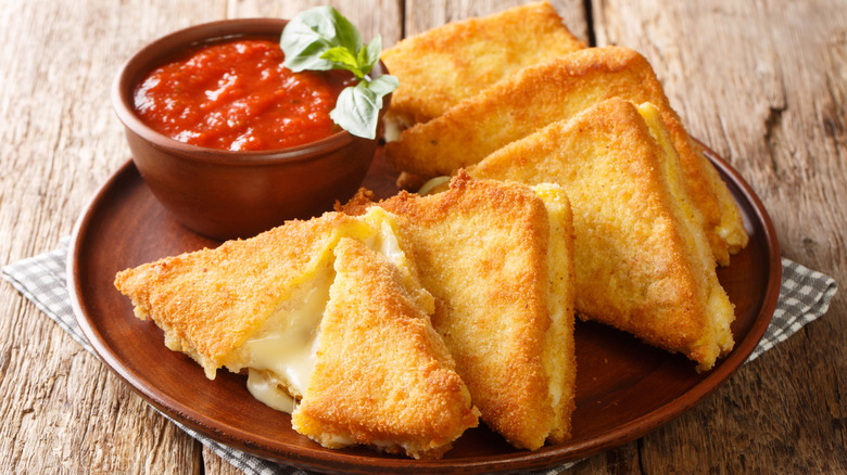 Mozzarella in carrozza on a brown plate with marinara dip in a bowl on a checkered cloth and wooden table