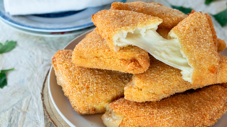 Mozzarella in carrozza on a plate atop a white table with leaves and another plate in the background