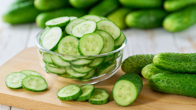 bowl of sliced cucumbers on a cutting board with whole cucumbers