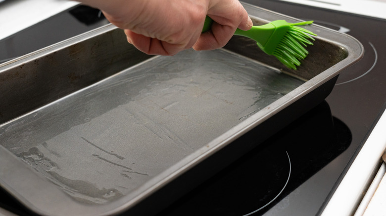 A hand brushing a sheet pan with oil 