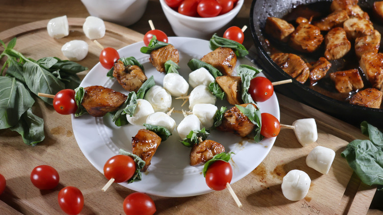 plate of Margherita chicken skewers on wooden cutting board next to skillet of glazed chicken