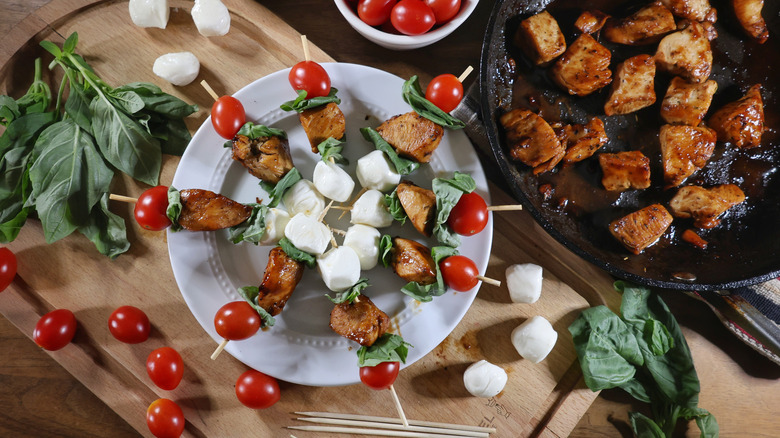 Margherita chicken skewers on plate on cutting board next to skillet of balsamic-glazed chicken