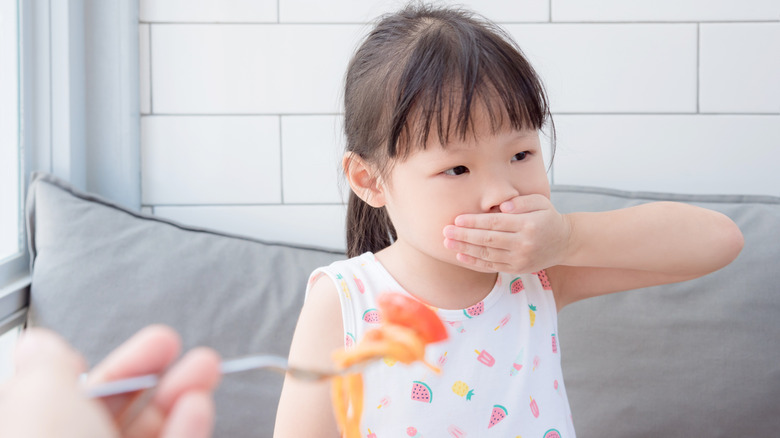 Little girl with a hand over her mouth refusing to eat a tomato