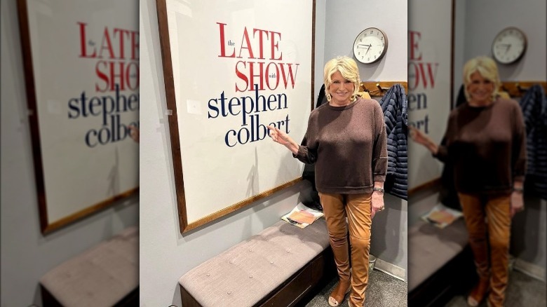 Martha Stewart sanding in front of a picture of the Late Show with Stephen Colbert poster