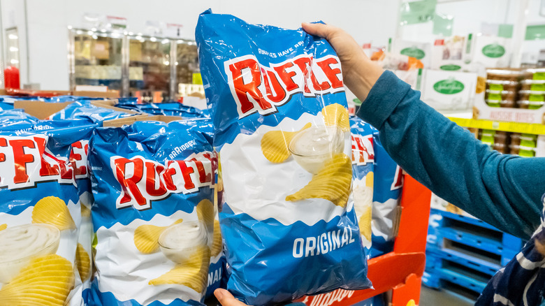 A person holds a bag of ruffles up in a supermarket