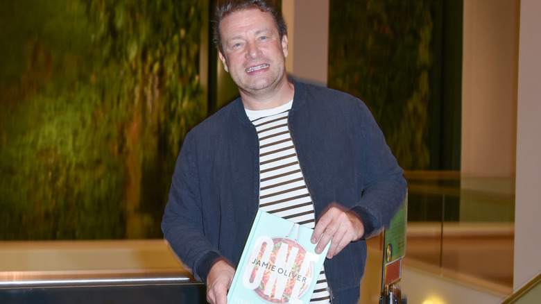 Jamie Oliver holding his cookbook "One"