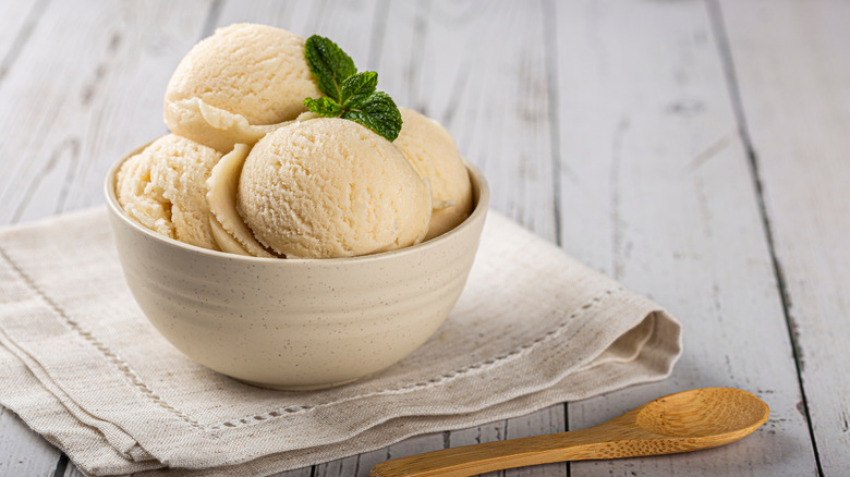 bowl of vanilla ice cream with mint garnish and wooden spoon