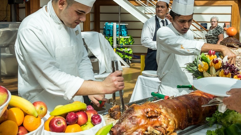 Chef carving meat on buffet line next to bowls of fruit