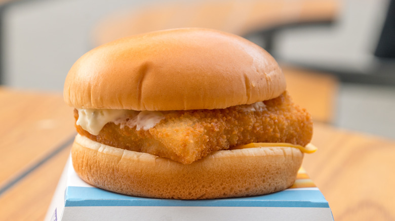 Filet-O-Fish atop container on wooden table with gray background