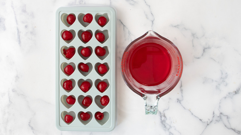 Maraschino cherries in heart-shaped ice cube mold slots next to measuring cup with cherry juice