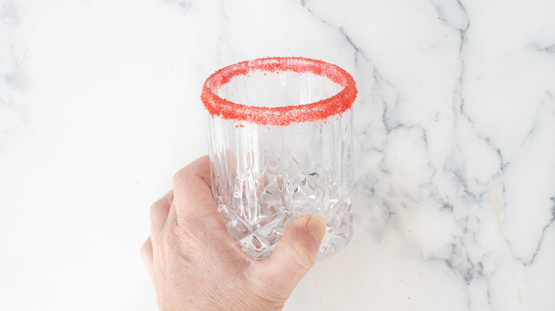 Hand holding glass rimmed with red sugar