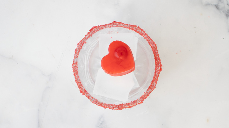 Red sugar-rimmed cocktail glass with ice and heart-shaped red ice cube