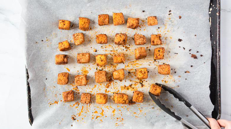 flipping tofu on baking sheet with tongs