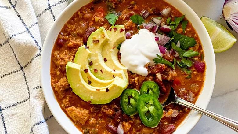 White bowl of chili with avocado