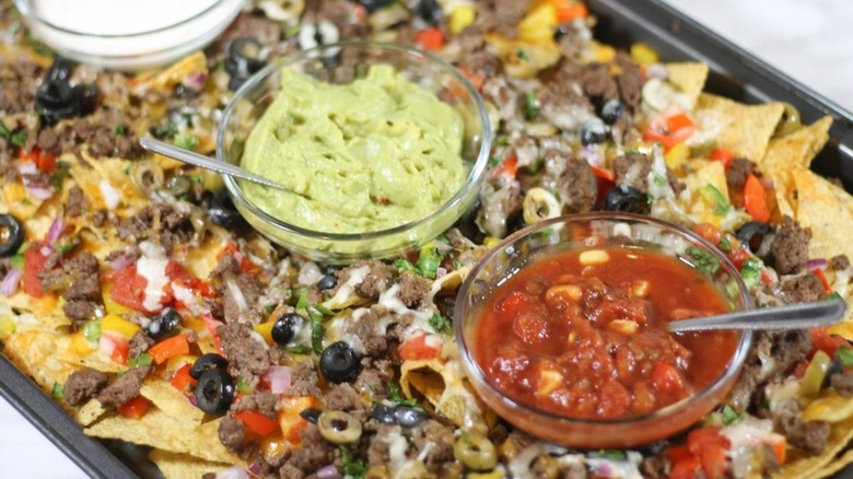 Baking sheet with nachos and bowls of toppings