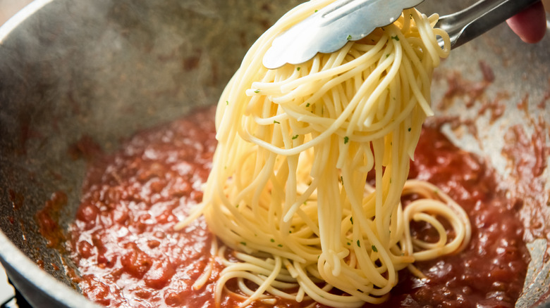 Tongs dropping spaghetti into a pan of sauce