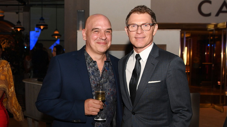 Michael Symon and Bobby Flay smiling at an event