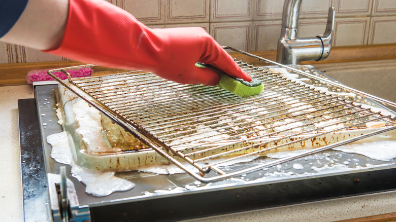 person cleaning oven grates over sink