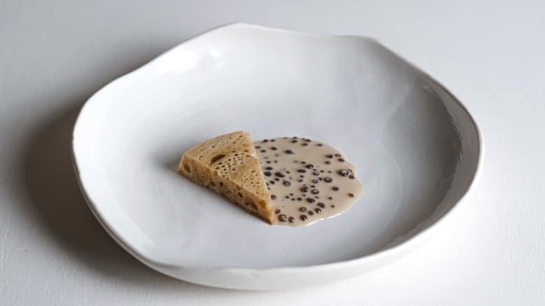 triangular piece of bread in a beige liquid with seaweed pearls