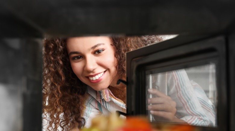 Happy woman opening a microwave 