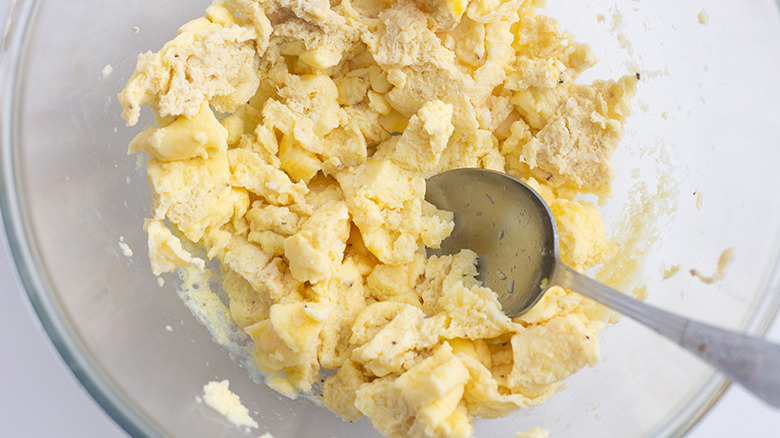 Overhead shot of a glass mixing bowl filled with scrambled eggs being stirred by a metal spoon