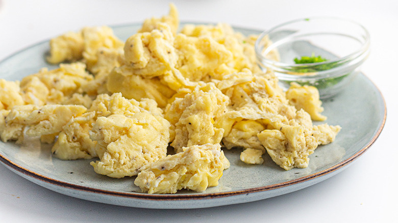 A plate of scrambled eggs with a small glass bowl of chives