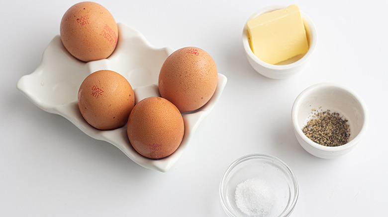 Four brown eggs next to containers of butter, salt, and pepper.