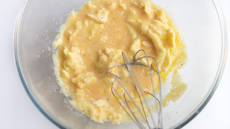 Partially cooked eggs in a glass mixing bowl being whisked