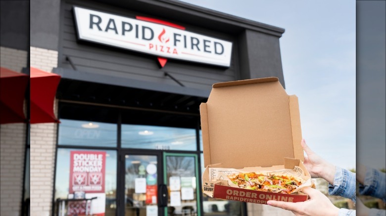 holding Rapid Fired pizza outside restaurant