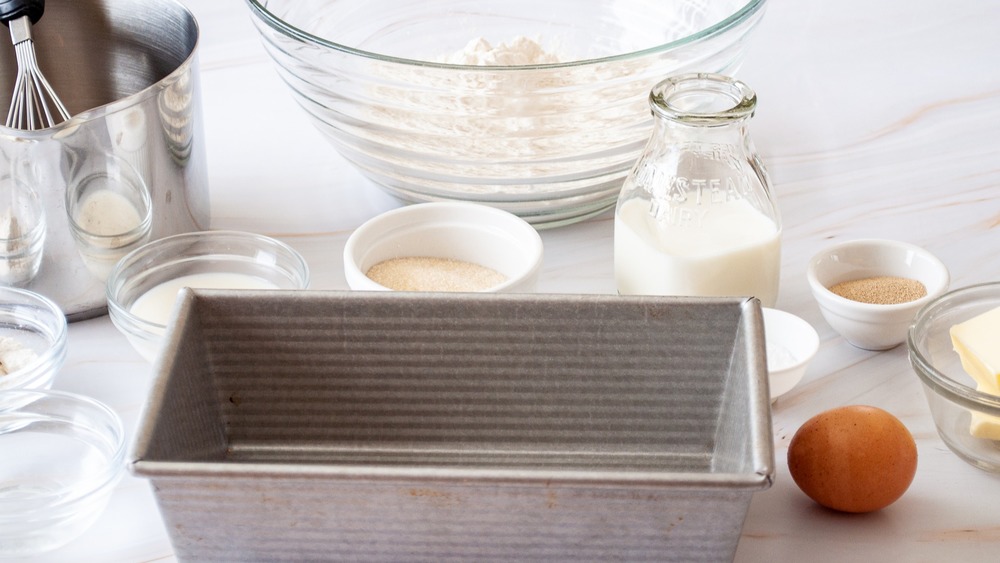 milk bread ingredients with whisk, pan, bowl and loaf pan