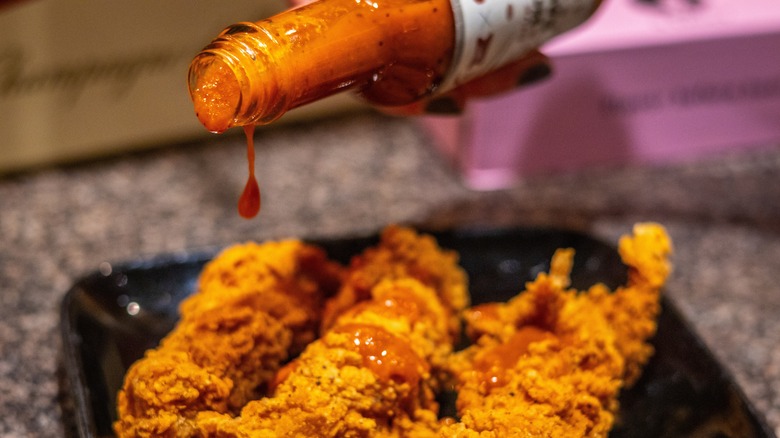 Pouring hot sauce on chicken fingers 