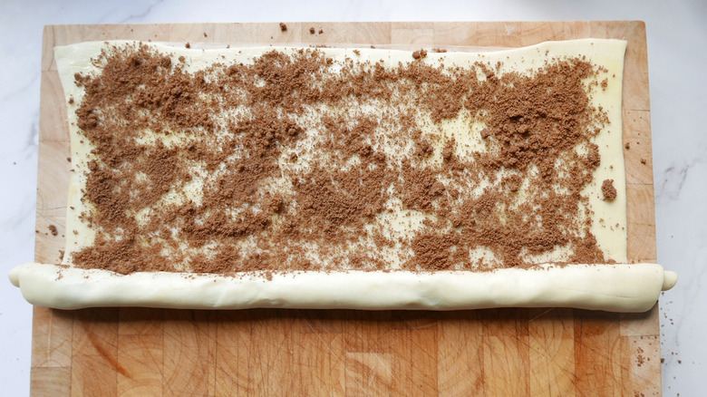 rolling up a Cinnamon roll cookie pie crust on cutting board