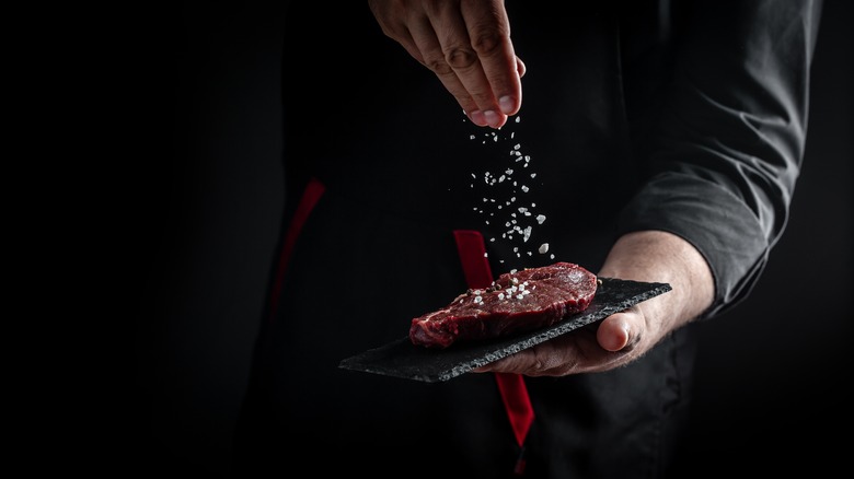 Chef sprinkling salt onto steak