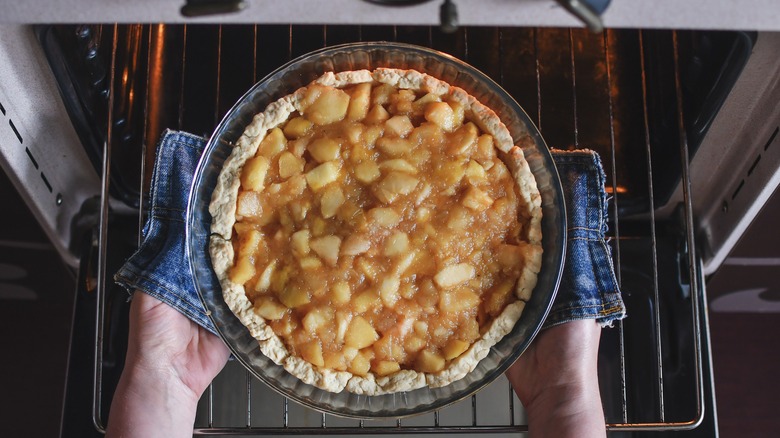 Hands putting apple pie in oven