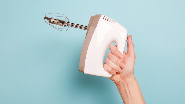 Hand holding a hand mixer on blue background