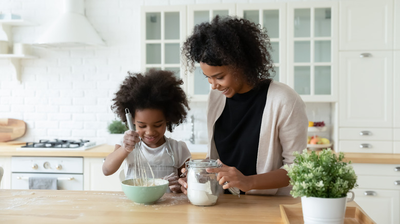 Woman and young girl mixing dough in kitchen
