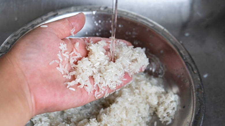 a hand rinsing rice under water in a sink