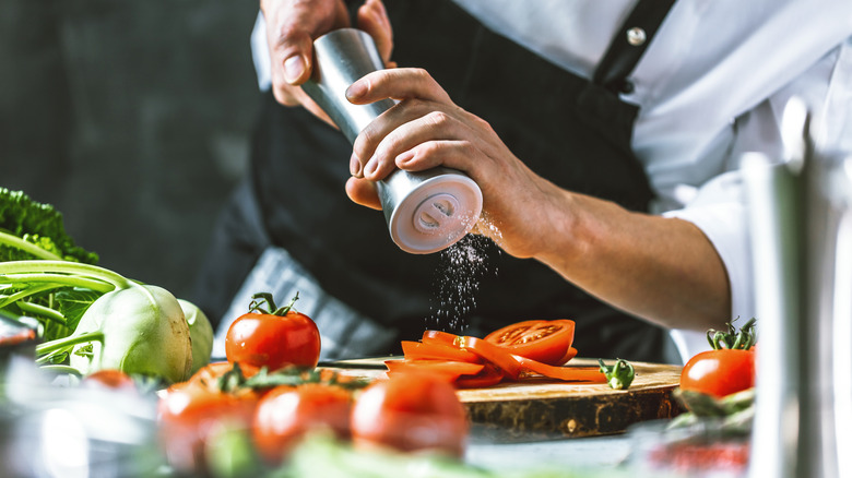 person salting sliced tomatoes