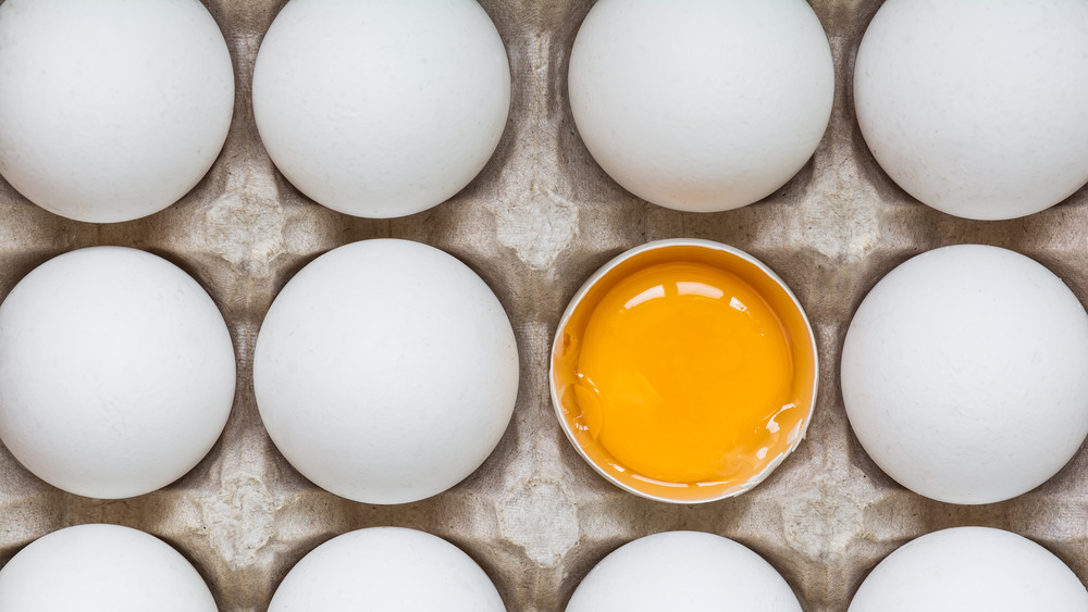 dozen white eggs with one cracked open 