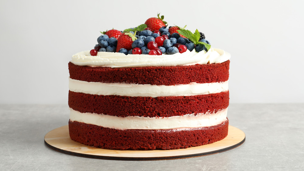 A red velvet cake topped with fresh fruit on a wooden cake board