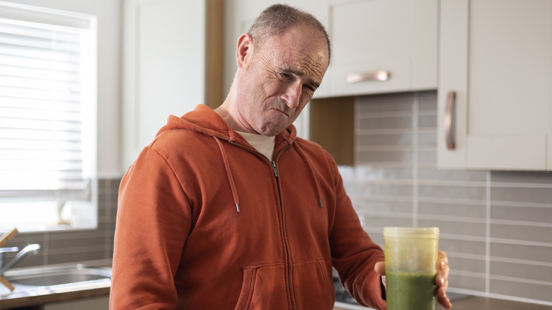 Grimacing man holding green drink