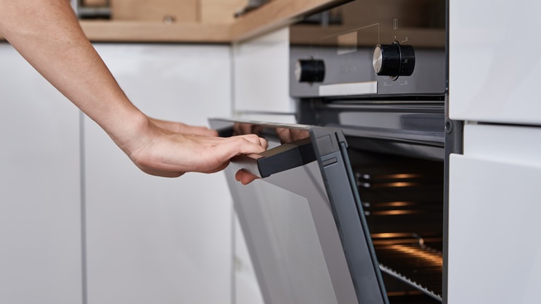 Woman hand open electric oven door with handle