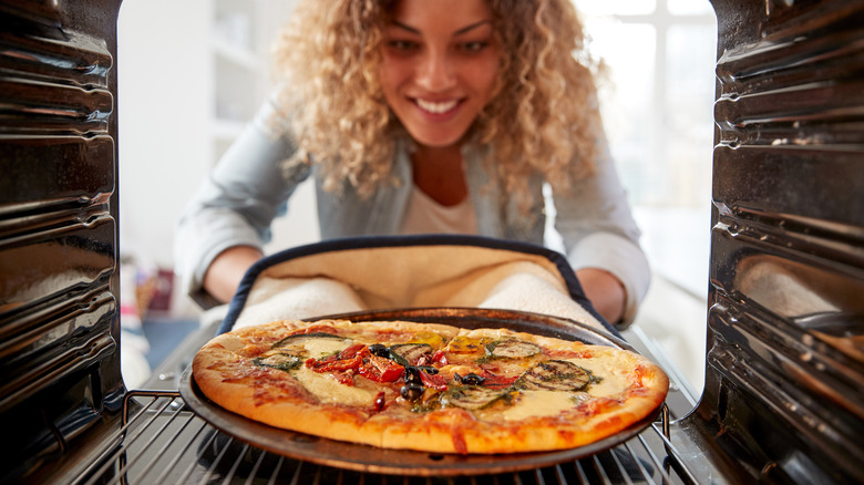 woman putting a pizza in the oven 