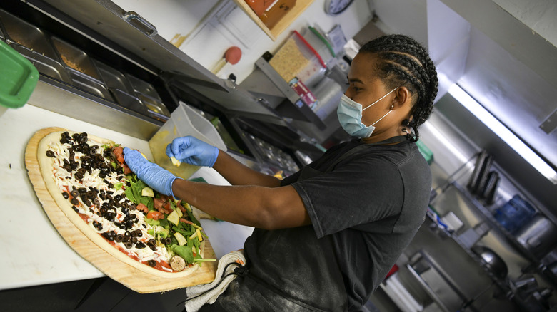 employee putting lots of toppings on a pizza